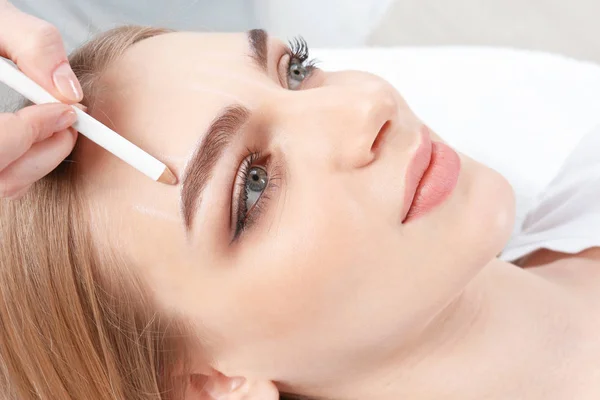 Cosmetólogo preparando a mujer joven para el procedimiento permanente del maquillaje de la ceja, primer plano —  Fotos de Stock