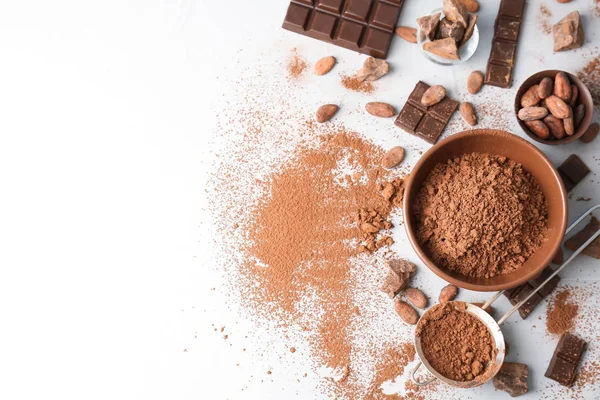 Flat lay composition with cocoa powder, beans and chocolate on light background