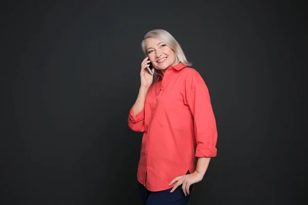 Зрелая женщина разговаривает по мобильному телефону на черном фоне — стоковое фото