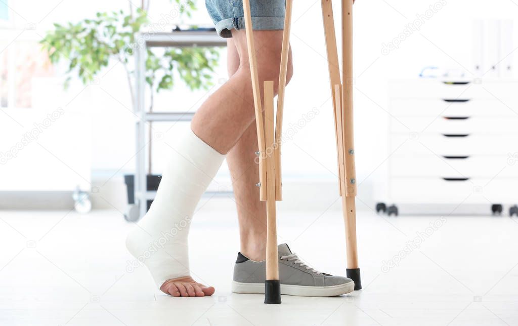 Man with broken leg in cast standing on crutches, indoors