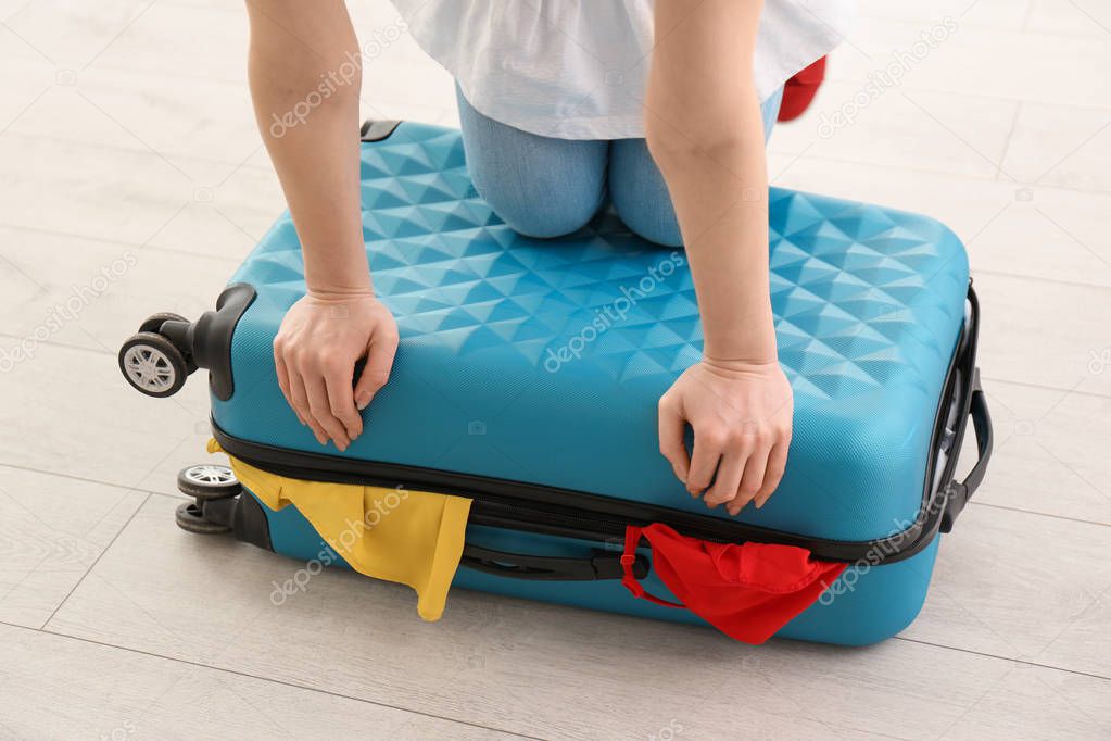 Young woman struggling to close suitcase indoors