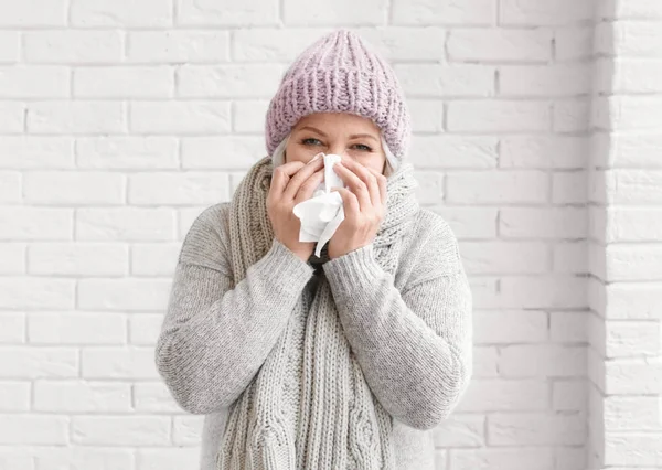 Зрелая женщина в теплой одежде, страдающая от холода на кирпичном фоне — стоковое фото