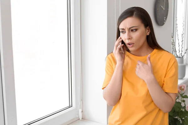 Mulher discutindo no telefone celular perto da janela em casa — Fotografia de Stock