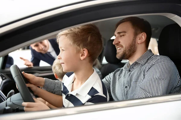 Familia joven eligiendo coche nuevo con vendedor en el salón — Foto de Stock