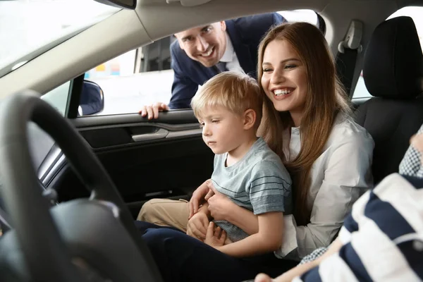 Familia joven eligiendo coche nuevo con vendedor en el salón — Foto de Stock