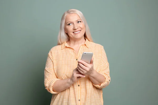 Mujer madura usando el teléfono móvil en el fondo de color —  Fotos de Stock