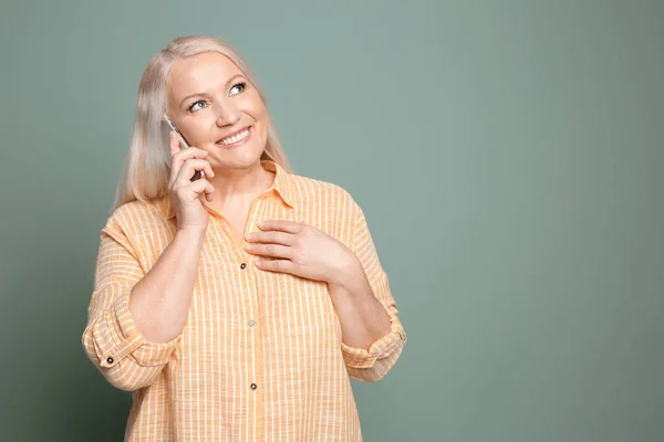 Mature woman talking on mobile phone against color background — Stock Photo, Image