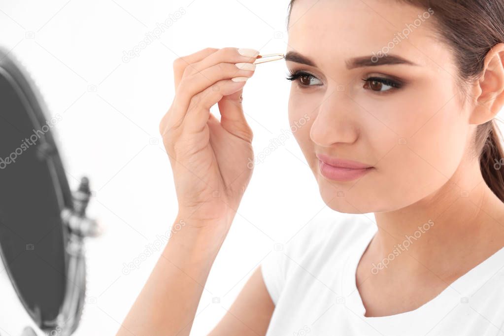 Young woman plucking eyebrow with tweezers, indoors