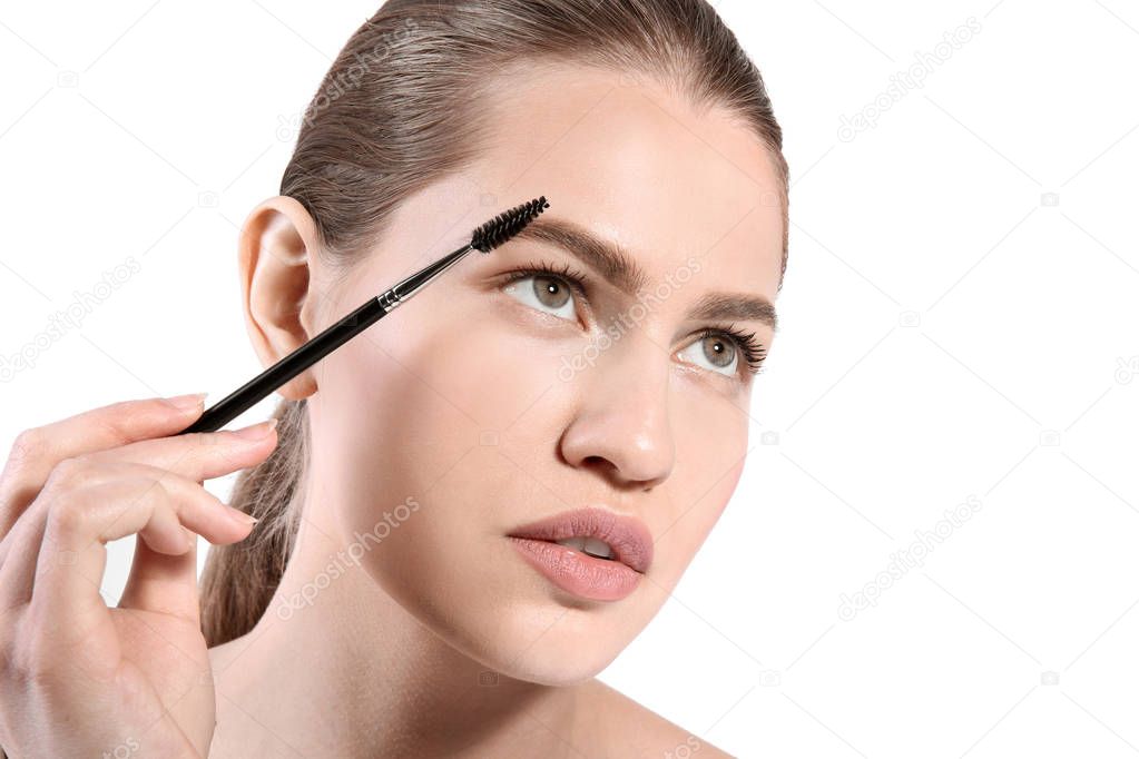 Beautiful woman with perfect eyebrows applying makeup on light background