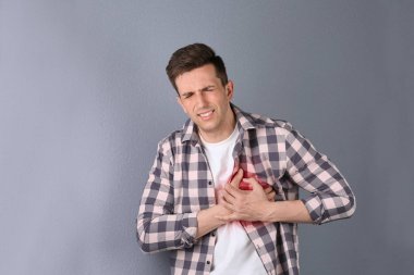 Young man having heart attack on color background clipart