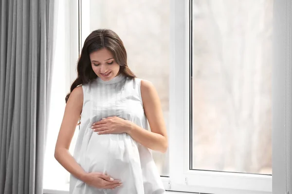 Mooie zwangere vrouw in de buurt van raam thuis — Stockfoto