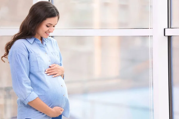 Piękna ciężarna kobieta w pobliżu okna w domu — Zdjęcie stockowe