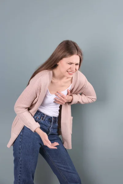 Young woman having heart attack on color background — Stock Photo, Image