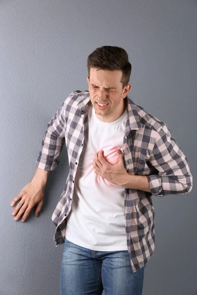 Hombre joven teniendo un ataque al corazón en el fondo de color — Foto de Stock