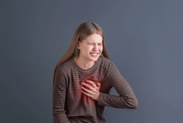 Mujer joven teniendo un ataque al corazón sobre fondo gris —  Fotos de Stock