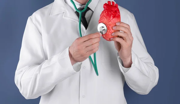 Médico sosteniendo modelo de corazón y estetoscopio sobre fondo de color. Prevenir un ataque al corazón — Foto de Stock