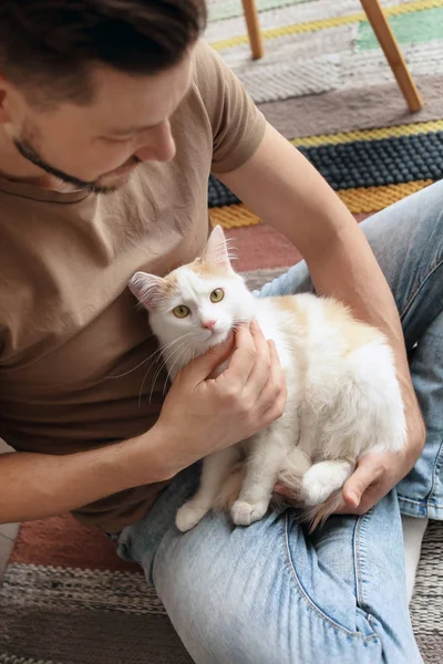 Молодой человек с симпатичной кошкой сидит на полу дома — стоковое фото