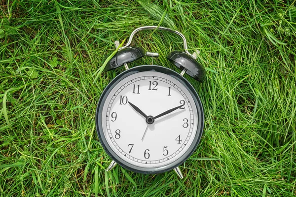 Reloj despertador en hierba verde, al aire libre. Concepto de cambio de tiempo —  Fotos de Stock