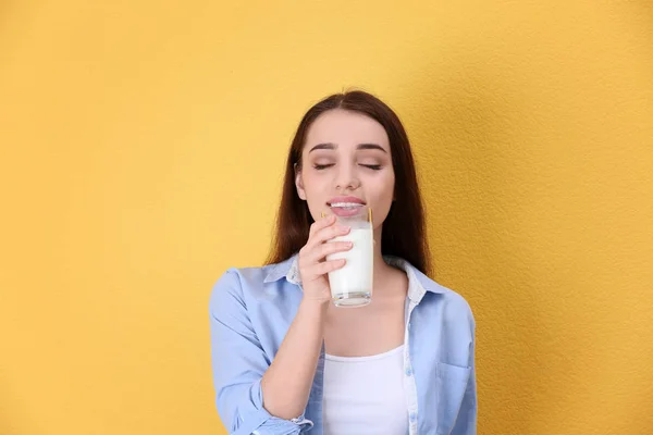Krásná mladá žena pití mléka na barevném pozadí — Stock fotografie