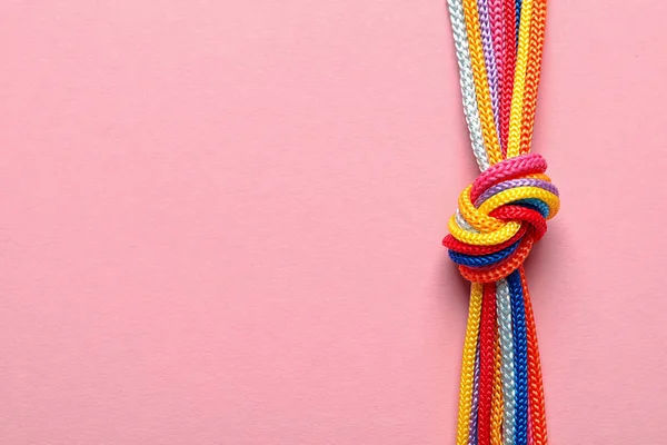Diferentes cuerdas atadas juntas con nudo sobre fondo de color. Concepto de unidad — Foto de Stock