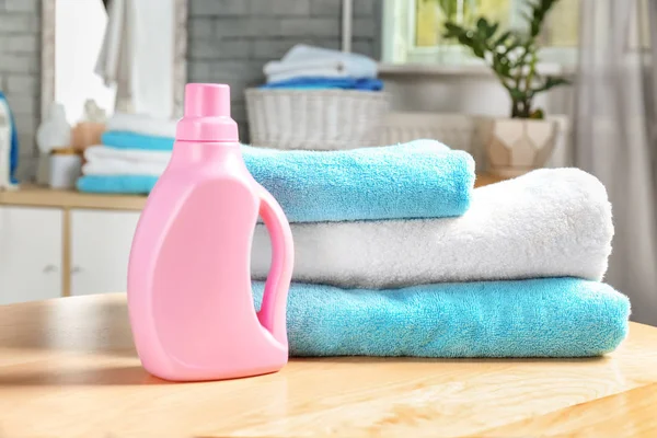 Pilha de toalhas limpas e garrafa com detergente na mesa — Fotografia de Stock