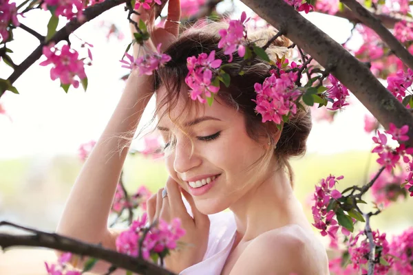 Attraente giovane donna posa vicino albero in fiore nella soleggiata giornata primaverile — Foto Stock