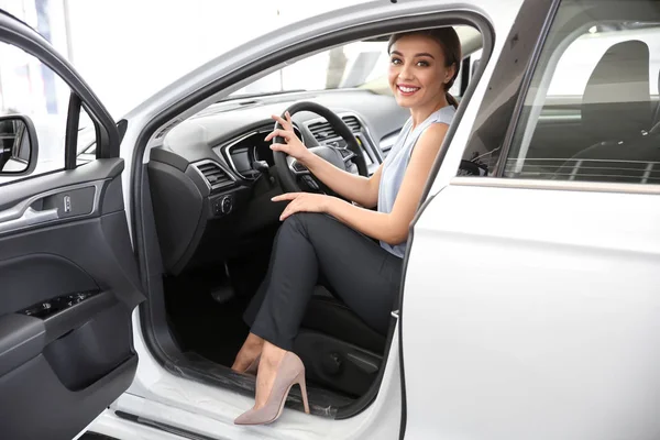 Mujer joven sentada en el asiento del conductor del coche nuevo en el salón — Foto de Stock