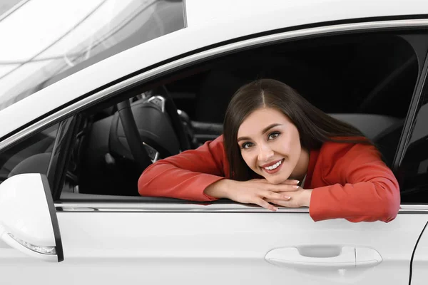 Νεαρή γυναίκα που κάθεται στο κάθισμα του οδηγού των νέων αυτοκινήτων στο σαλόνι — Φωτογραφία Αρχείου