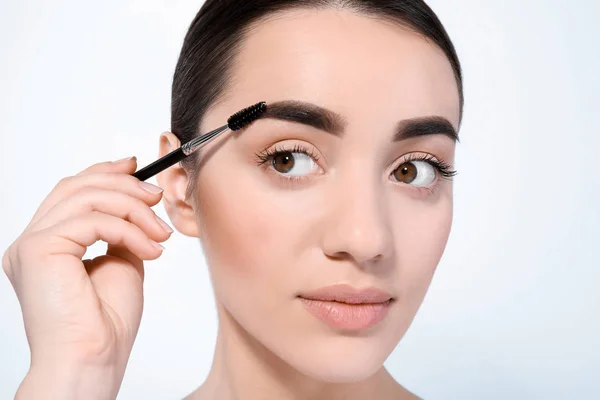 Mulher bonita com sobrancelhas perfeitas aplicando maquiagem no fundo claro — Fotografia de Stock