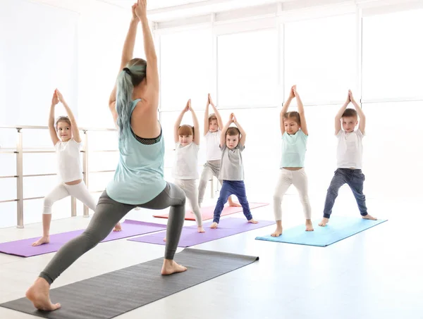 Los niños pequeños y su profesor practican yoga en el gimnasio —  Fotos de Stock
