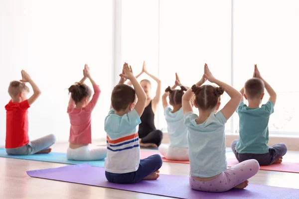 Los niños pequeños y su profesor practican yoga en el gimnasio —  Fotos de Stock