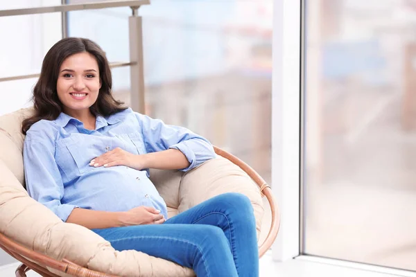 Mulher grávida bonita sentada na cadeira lounge perto da janela — Fotografia de Stock