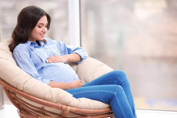 Piękne kobiety w ciąży, siedząc w fotelu w pobliżu okna — Zdjęcie stockowe