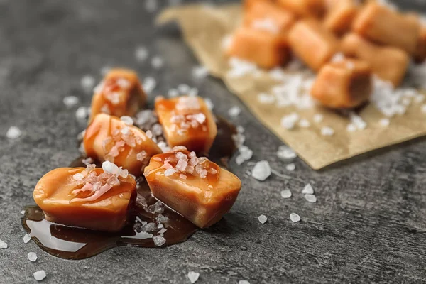 Doces deliciosos com molho de caramelo e sal no fundo cinza — Fotografia de Stock