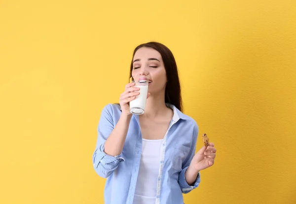 Hermosa mujer joven bebiendo leche con galletas en el fondo de color — Foto de Stock