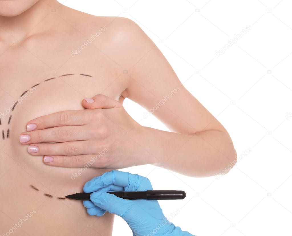 Doctor drawing marks on female breast for cosmetic surgery operation against white background, closeup
