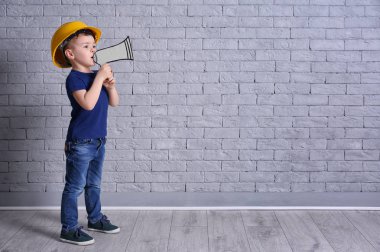 Kask ile kağıt megafon tuğla duvar arka plan üzerinde sevimli küçük çocuk