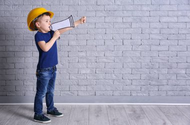 Kask ile kağıt megafon tuğla duvar arka plan üzerinde sevimli küçük çocuk