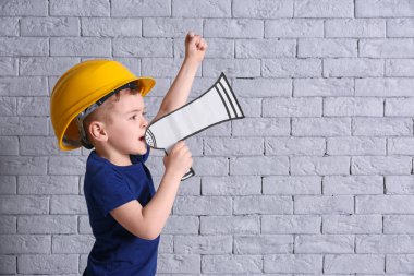 Kask ile kağıt megafon tuğla duvar arka plan üzerinde sevimli küçük çocuk