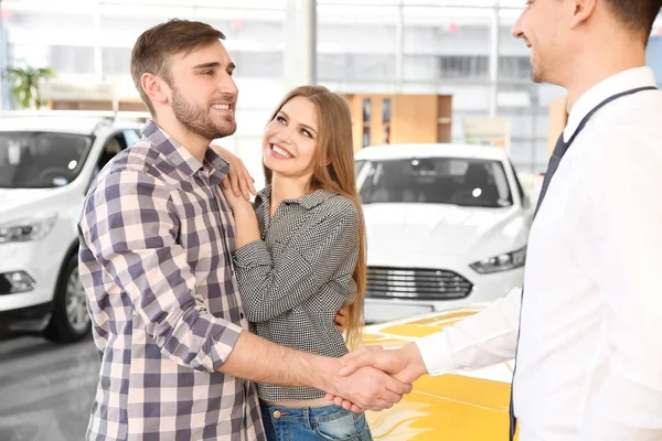 Mladý muž potřásl rukou s prodejcem v autosalonu — Stock fotografie