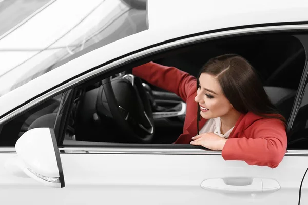 Jovem mulher sentada no assento do motorista do carro novo no salão — Fotografia de Stock