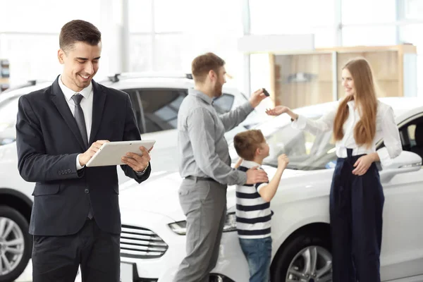 Vendedor con tablet y familia joven en salón de coches —  Fotos de Stock