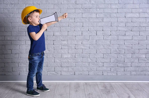 Adorabile bambino in hardhat con megafono di carta su sfondo muro di mattoni — Foto Stock
