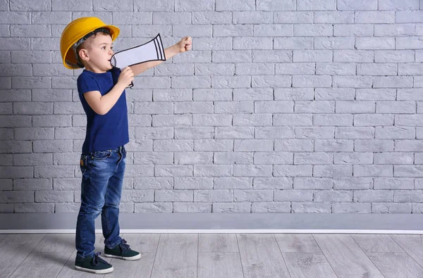 Kask ile kağıt megafon tuğla duvar arka plan üzerinde sevimli küçük çocuk