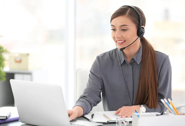 Mujer joven hablando por teléfono a través de auriculares en el lugar de trabajo —  Fotos de Stock