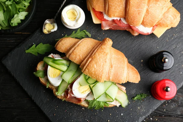 Leckere Croissant-Sandwiches mit Speck auf dunklem Hintergrund, Draufsicht — Stockfoto