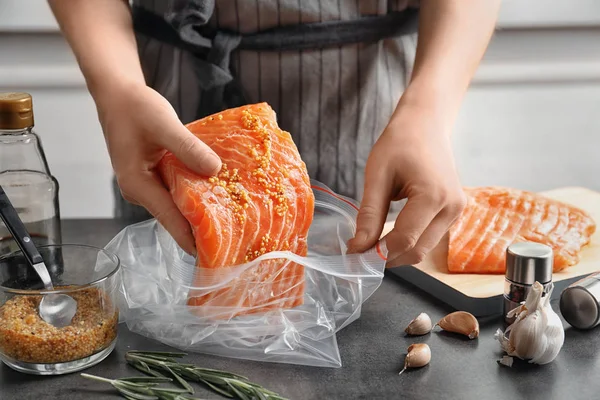 Frau legt mariniertes Lachsfilet in Plastiktüte am Tisch — Stockfoto