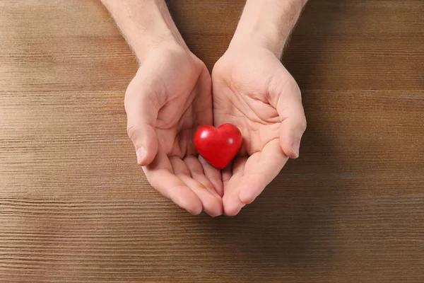 Мужчина держит маленькое красное сердце на деревянном столе. Концепция сердечного приступа — стоковое фото