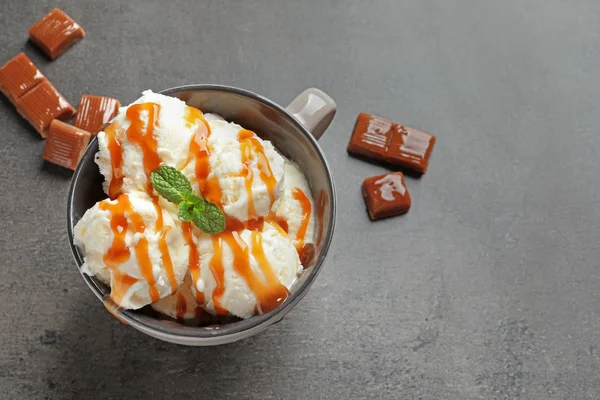 Gelato saporito con salsa al caramello in tazza e caramelle in tavola — Foto Stock