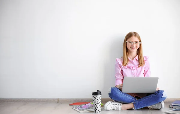 Blogueur adolescent mignon avec ordinateur portable assis sur le sol contre un mur léger — Photo